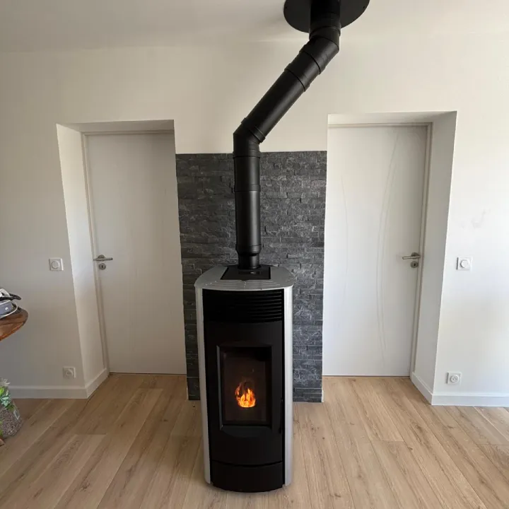 Poêle à bois à granulés installé dans un salon moderne gris par Alpes Chauffage Confort.